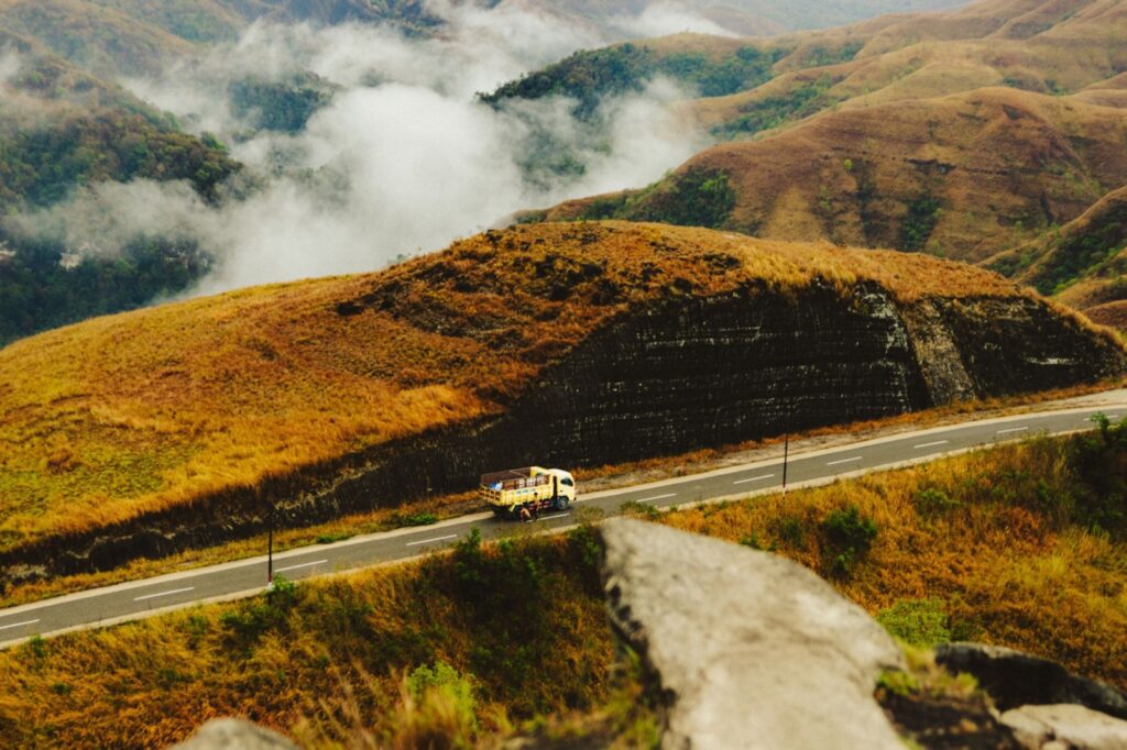 Vrachtwagen op de weg tussen goudkleurige heuvels en wolken op Sumba
