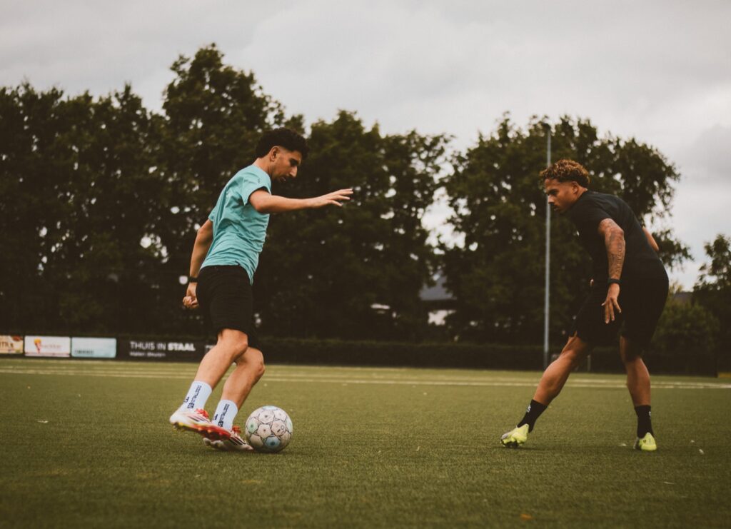 Speler in turquoise shirt dribbelt op zijn tegenstander af
