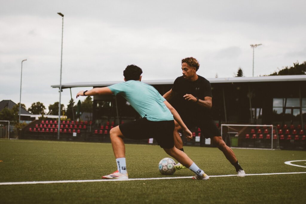 Speler in zwart passeert zijn tegenstander bij de tribune